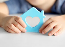 Child Holding Figure In Shape Of House, Closeup. Adoption Concep